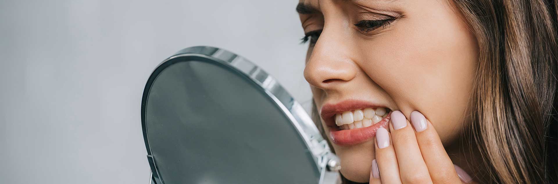 Close-up view of young woman having toothache and looking at mirror